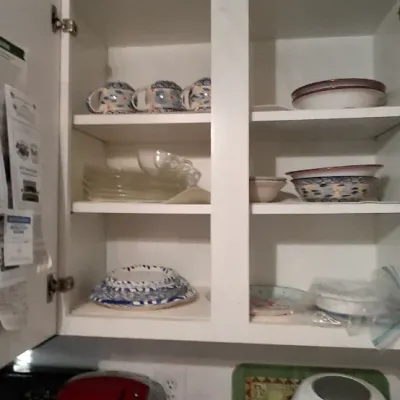 Sale Photo Thumbnail #49: Open white kitchen cabinet filled with assorted glassware, blue and white patterned china, and serving bowls, above small countertop appliances including a red coffee maker and a white air fryer.
