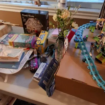 Sale Photo Thumbnail #113: Assorted craft and play items on a table, including a Robotime Flower House miniature kit, a toy roller coaster set, Crayola paints, and stationary.