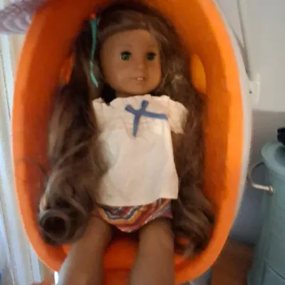 Sale Photo Thumbnail #13: American Girl doll with long wavy brown hair seated in an orange pod-style chair accessorized with a floral sun hat.