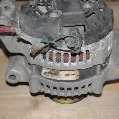 Used automotive alternator with attached wiring harness segment, showing typical wear and surface oxidation.