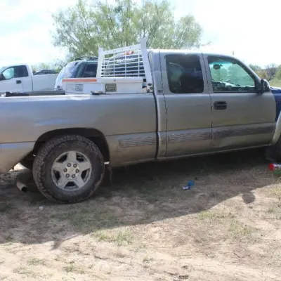 Silver Chevrolet Silverado pickup truck with extended cab, bed rack, and a mismatched blue front panel, showing visible wear and minor...