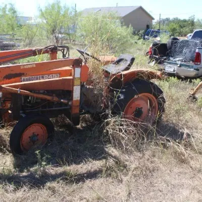Vintage orange Kubota L245 tractor with front loader attachment, showing weather wear and surface rust, parked outdoors in tall grass.