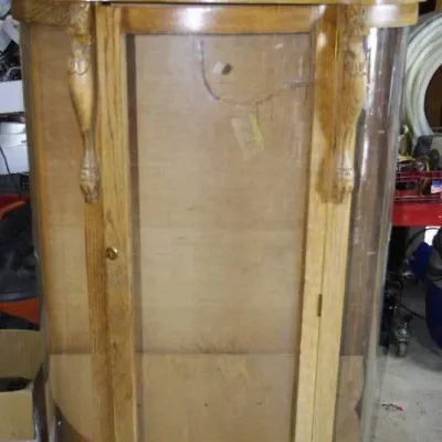 Vintage golden oak curved glass curio display cabinet with carved crest and lions head details.