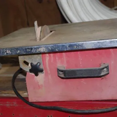 Portable benchtop wet tile saw featuring a metal table top, red housing with a side handle, and tilt adjustment.