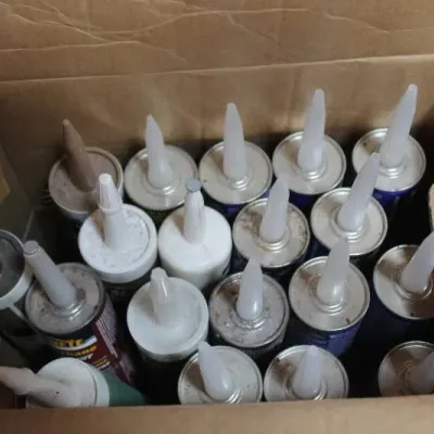 Cardboard box filled with assorted used and unused caulk and construction sealant tubes.