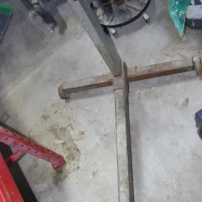 Heavy-duty steel engine stand on a wheeled base, showing surface wear and light rust from garage use.
