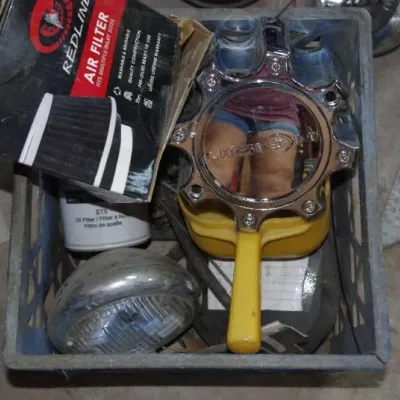 Plastic crate filled with assorted automotive parts including a chrome Vision Wheel center cap, a boxed Redline air filter, and a vintage...