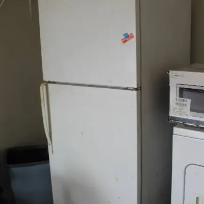 White top-freezer refrigerator showing minor exterior surface wear and scuffs, situated in a garage setting.