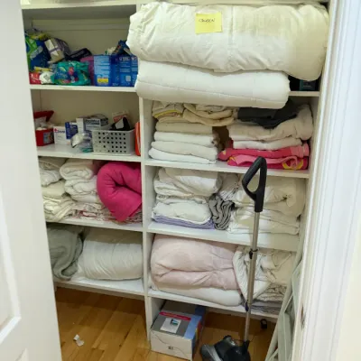 Sale Photo Thumbnail #73: Walk-in linen closet filled with assorted bedding, towels, blankets, and household supplies, alongside a upright vacuum cleaner.
