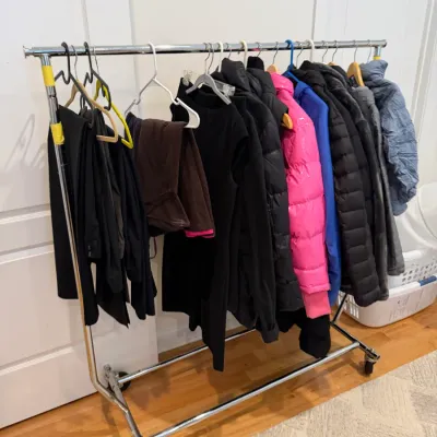 Sale Photo Thumbnail #66: Rolling chrome garment rack holding an assortment of outerwear, including puffer jackets, coats, and pants.