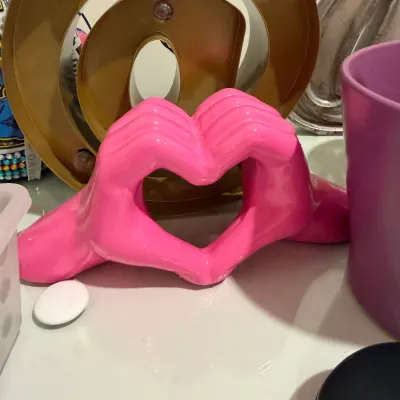 Sale Photo Thumbnail #82: Glossy hot pink resin sculpture of hands forming a heart, displayed alongside decorative homeware items.