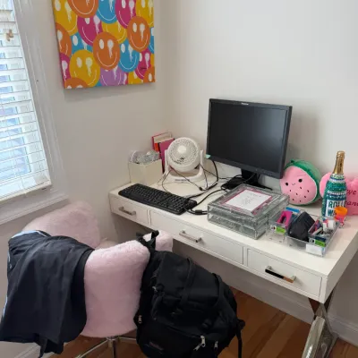 Sale Photo Thumbnail #99: White writing desk with chrome X-legs paired with a pink faux-fur swivel office chair, alongside computer equipment and colorful smiley face wall art.
