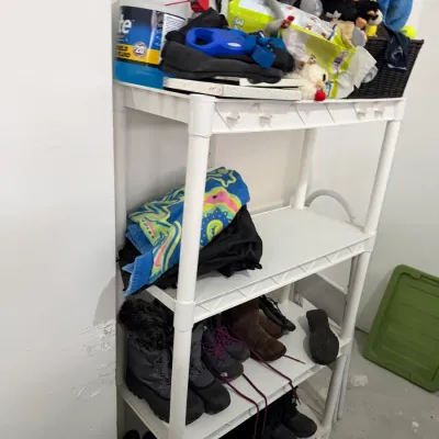 Sale Photo Thumbnail #43: White plastic four-tier shelving unit holding various household items, including winter boots, shoes, towels, and garage supplies.