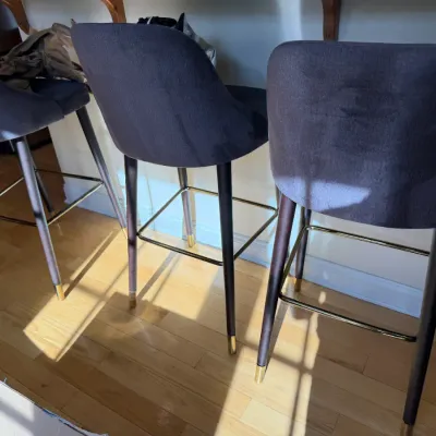 Sale Photo Thumbnail #32: Set of three modern upholstered barstools featuring dark grey fabric seats, dark wooden legs, and brass-tone metal footrests and leg tips.