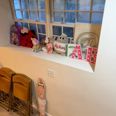 Sale Photo Thumbnail #45: Collection of children's stuffed toys, decorative marquee letters, and backpacks displayed on a windowsill, alongside stacked gold metal folding chairs.