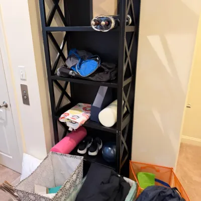 Sale Photo Thumbnail #93: Tall black wood shelving unit with X-brace sides, holding various household items, fitness gear, and storage bins.