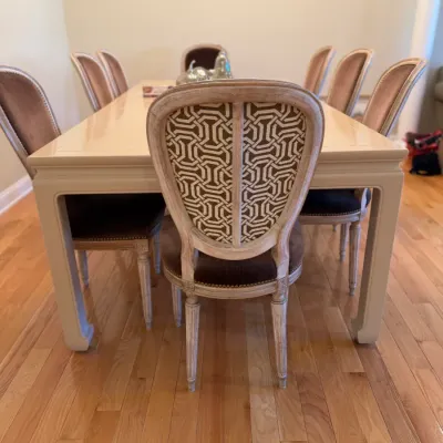Sale Photo Thumbnail #19: French Country style dining set featuring a cream-colored rectangular table and eight upholstered chairs with distressed whitewashed wooden frames.