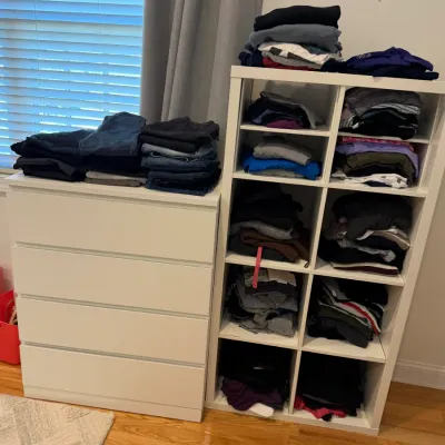 Sale Photo Thumbnail #59: White four-drawer dresser and matching eight-cube shelf unit filled with stacks of folded clothing.