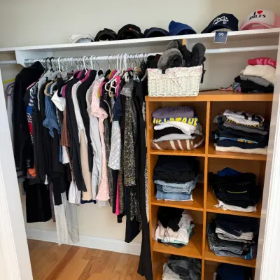 Sale Photo Thumbnail #101: Closet filled with women's hanging clothing, folded apparel, baseball caps on a top shelf, and a wooden cubby storage unit.