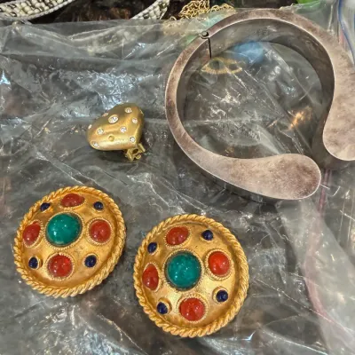 Sale Photo Thumbnail #31: Collection of vintage costume jewelry, including a pair of gold-tone cabochon clip-on earrings, a heart-shaped clip, a silver-tone hinged cuff bracelet, and beaded necklaces.