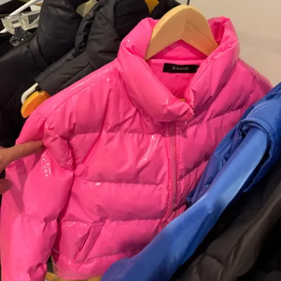 Sale Photo Thumbnail #69: Bright hot pink glossy cropped puffer jacket by AIWENDY hanging on a rack among other winter coats.