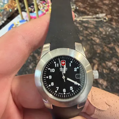Sale Photo Thumbnail #28: Swiss Army wristwatch featuring a black dial, Arabic numerals, date window, brushed stainless steel case, and a black rubber strap.