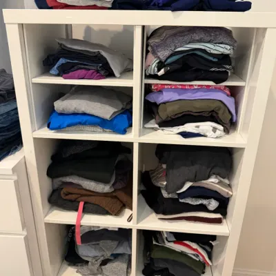 Sale Photo Thumbnail #58: White wooden cubby shelving unit filled with stacks of assorted neatly folded casual clothing.