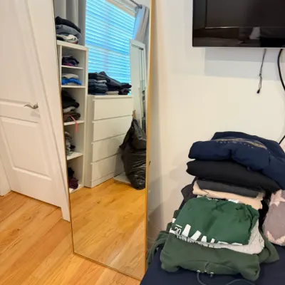 Sale Photo Thumbnail #65: Tall full-length floor mirror with a thin gold-tone metal frame, displayed alongside a stack of folded sweatshirts.