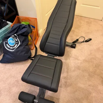 Sale Photo Thumbnail #92: Adjustable weight bench with black faux-leather padded upholstery, red stitching, and integrated leg rollers and resistance band attachments.