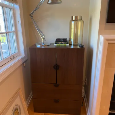 Sale Photo Thumbnail #2: Modern dark wood cabinet with lower drawers, topped with a chrome adjustable task lamp and decorative accessories.