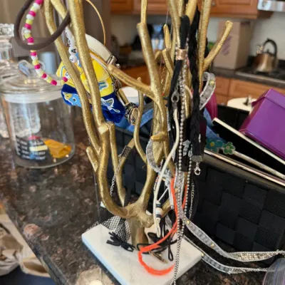 Sale Photo Thumbnail #30: Gold-painted tree-shaped jewelry stand mounted on a white marble base, holding assorted fashion necklaces, hair ties, and bracelets.