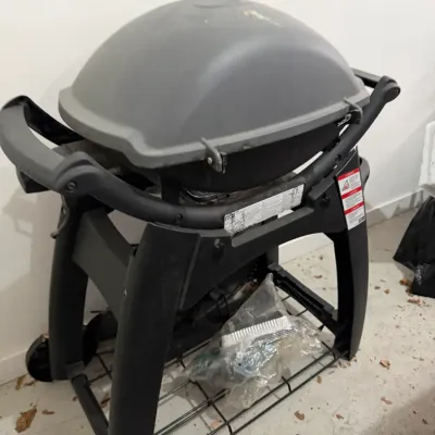 Sale Photo Thumbnail #44: Weber Q series liquid propane gas grill on a rolling cart stand, featuring a grey lid and black frame.
