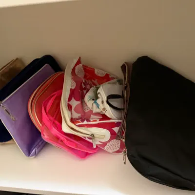 Sale Photo Thumbnail #74: Collection of modern zippered makeup pouches and small travel bags resting on a white shelf.