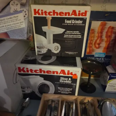 Sale Photo Thumbnail #96: Vintage boxed KitchenAid stand mixer attachments, including a Food Grinder (FGA) and a Slicer & Shredder, alongside various kitchen items and flatware.