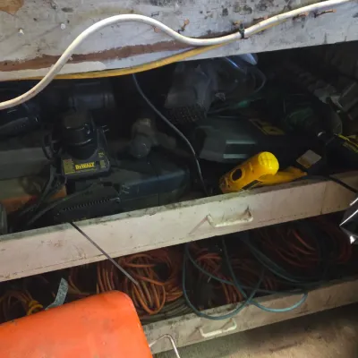 Sale Photo Thumbnail #48: Assorted power tools, battery chargers, and heavy-duty extension cords stored on workbench shelves.