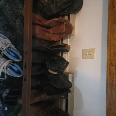 Sale Photo Thumbnail #130: Collection of various men's leather cowboy boots and sneakers displayed along a floor, showing wear from use.