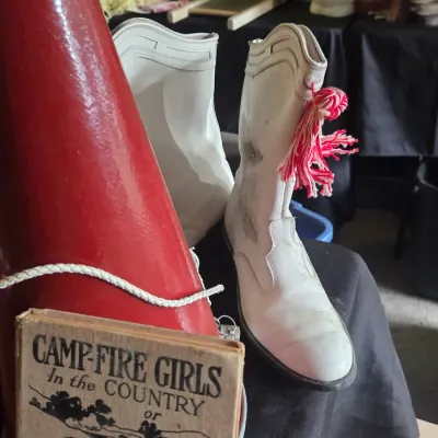 Sale Photo Thumbnail #54: Vintage white go-go or majorette boots with pink and white tassels, displayed alongside a red cheerleader megaphone and a Camp-Fire Girls book.