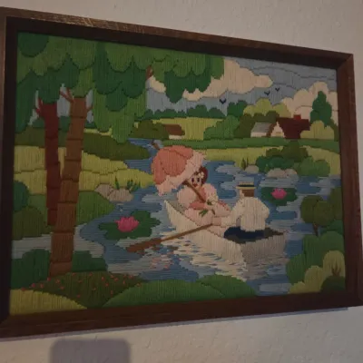 Sale Photo Thumbnail #87: Framed needlepoint art depicting a romantic couple boating along a river, presented in a simple dark wood frame.