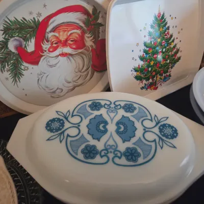 Sale Photo Thumbnail #117: Vintage Corning Ware oval casserole dish with a blue floral pattern lid, displayed alongside vintage Christmas serving trays featuring Santa Claus and a Christmas tree.