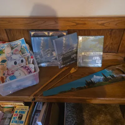 Sale Photo Thumbnail #88: Wooden bench featuring photo albums, a hand-painted handsaw, crafting supplies, and a plastic storage bin filled with books and decorations.