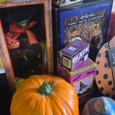 Sale Photo Thumbnail #36: Collection of vintage Halloween decorations, including a boxed animated witch figure, a large faux pumpkin, fabric mache scarecrows, and a black light bulb.