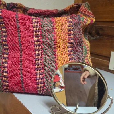 Sale Photo Thumbnail #6: Handwoven colorful tote bag in vibrant red, green, and yellow chevron patterns, paired with a small round brass vanity mirror on a scrollwork stand.