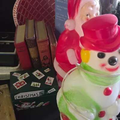 Sale Photo Thumbnail #38: Vintage plastic blow mold Santa and snowman figures displayed alongside old hardbound books and a green wooden Christmas card list box.