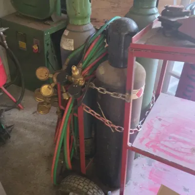 Sale Photo Thumbnail #13: Oxy-acetylene welding rig set, including compressed gas tanks, dual gauges, hoses, and a red metal rolling cart.