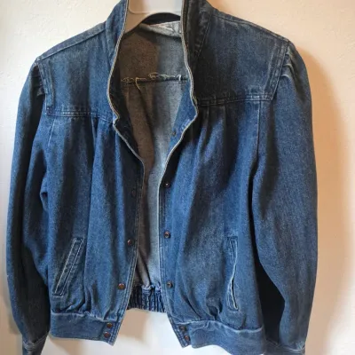 Sale Photo Thumbnail #128: Vintage 1980s medium-wash denim jacket featuring a snap-button front, elasticized waistband, and pleated shoulders.