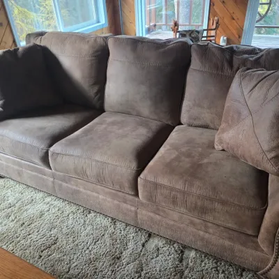 Sale Photo Thumbnail #78: Brown suede three-cushion sofa with nailhead trim detailing along the rolled arms and base, accompanied by matching throw pillows.