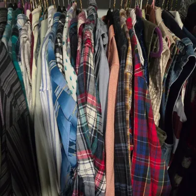 Sale Photo Thumbnail #145: Closet rack packed with vintage long-sleeve button-down shirts, featuring various plaid, striped, and solid patterns.