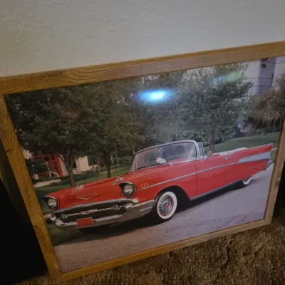 Sale Photo Thumbnail #91: Framed photograph of a classic red 1957 Chevrolet Bel Air convertible, housed in a light oak wooden frame.