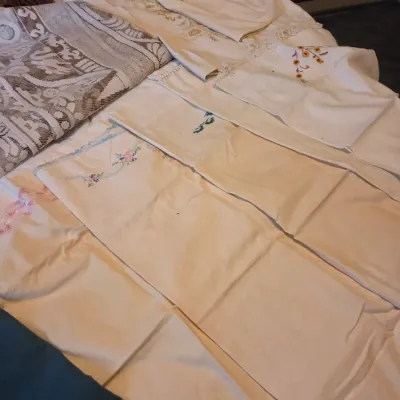 Sale Photo Thumbnail #121: Collection of vintage embroidered linens and table runners spread across a surface, featuring floral needlework and lace trim.