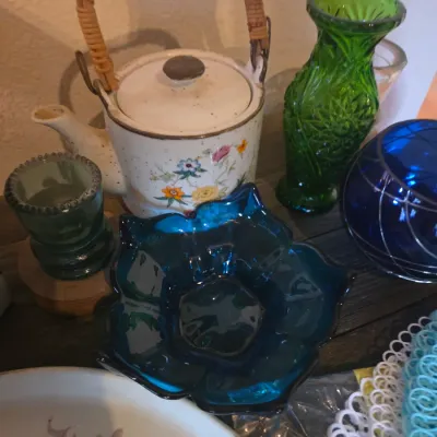 Sale Photo Thumbnail #99: Collection of vintage glassware and ceramics, including a floral speckled teapot with a wicker handle, green pressed glass vase, blue glass dish, and decorative glass orb.
